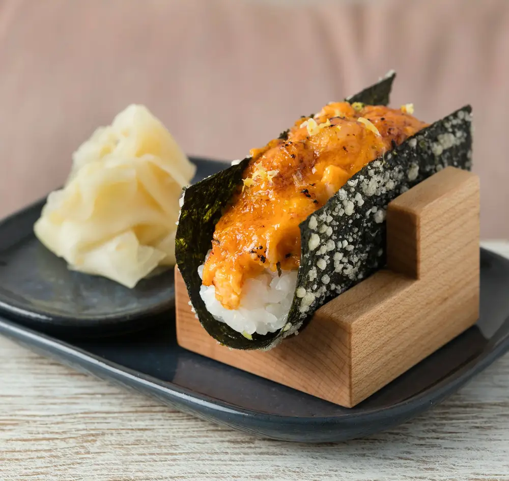 Hand roll plated in a wood holder at a restaurant table